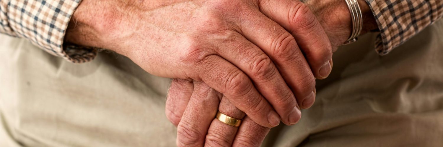 A detailed image of elderly hands clasping a wooden cane, symbolizing aging and support.